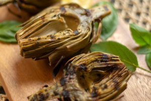 Close up shot of Grilled Artichokes on a Cutting Board with Basil and Sage
