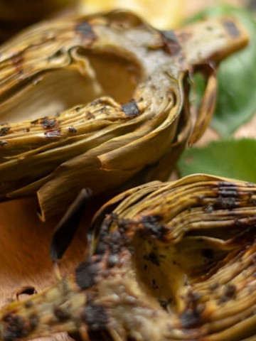 Close up shot of Grilled Artichokes on a Cutting Board with Basil and Sage