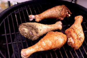 Four turkey legs resting on the grate over indirect heat on the Big Green Egg Charcoal Grill