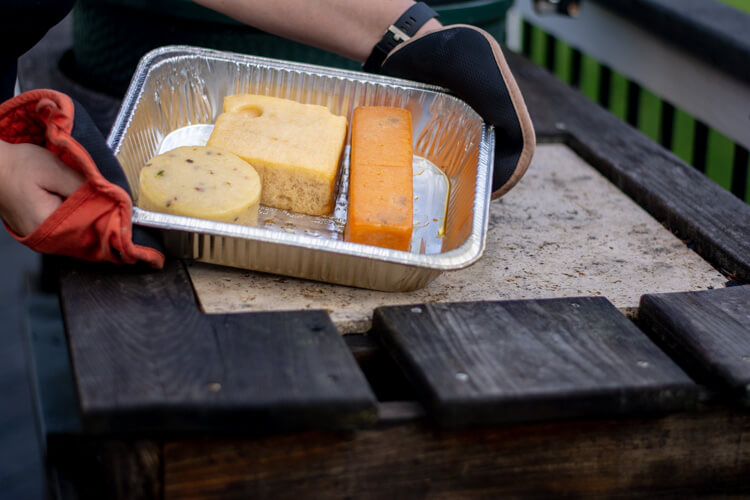 Three large blocks of cheese in a disposable pan on the big green egg table. The cheese is fully smoked and needs to cool