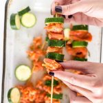 hands holding a skewer with salmon and zucchini to make kabobs