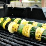 Marinated zucchini and yellow squash on a metal skewer on the grill