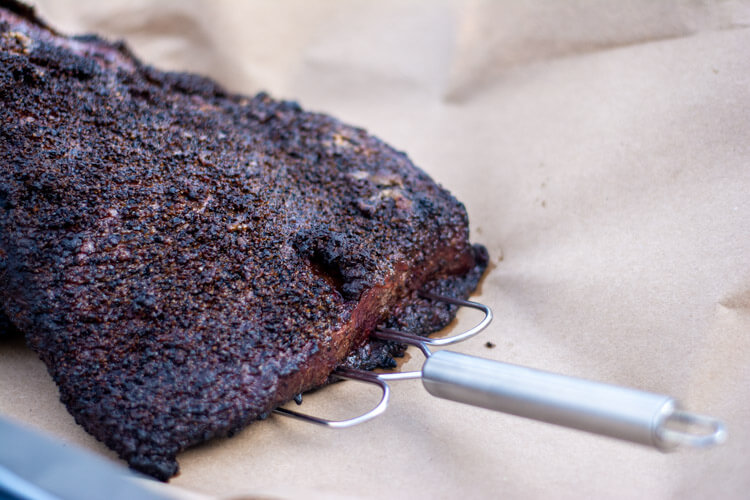 closeup of the gorgeous dark crust of the brisket with a meat claw on the butcher paper