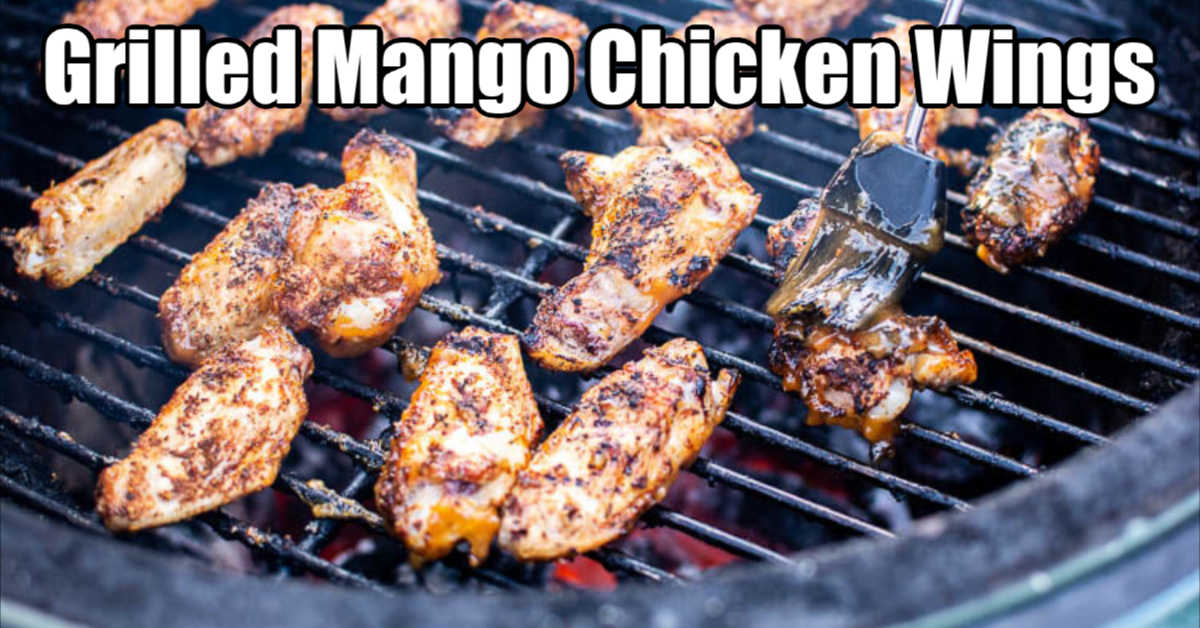 grilled mango chicken wings on the grill and being brushed with a sweet, tropical sauce