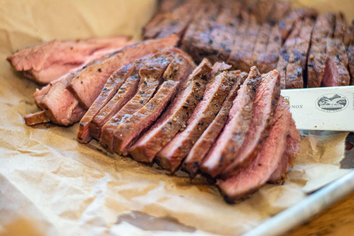sliced ranch steak on butcher paper lined sheet pan.