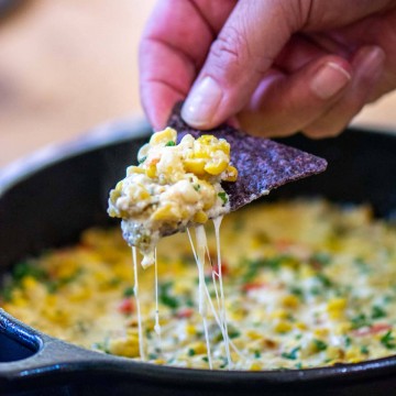 scooping the dip from the cast iron pan with strings of cheese