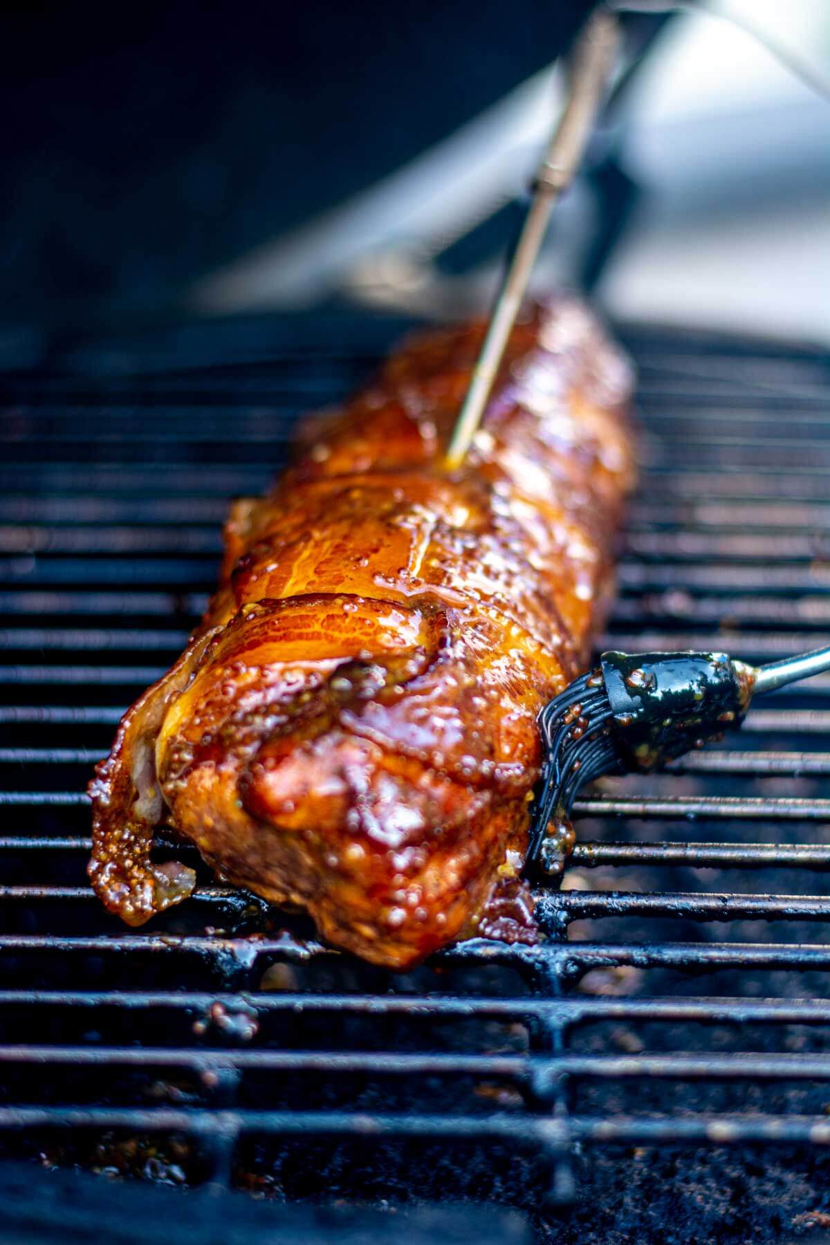 pork tenderloin is wrapped in bacon and being brushed with a honey mustard glaze.