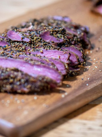 slices of goose breast on a cutting board coasted in the pastrami seasoning.