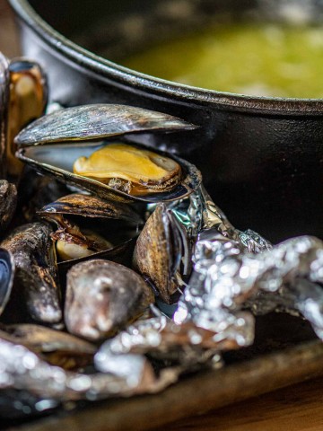 grilled mussels in a foil pack in front of melted butter.