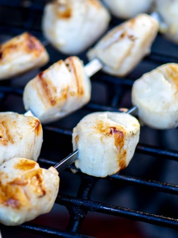 perfectly grilled scallops on skewers over the direct flame of the grill.