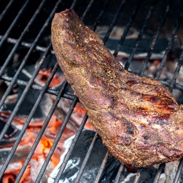 seared tri tip over hot glowing coals on the grill grate.