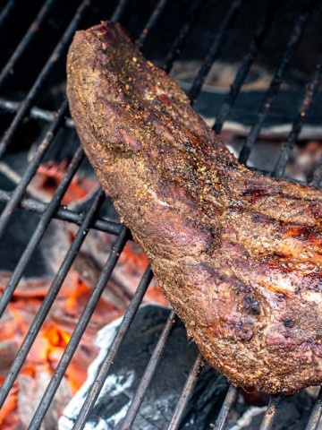 seared tri tip over hot glowing coals on the grill grate.