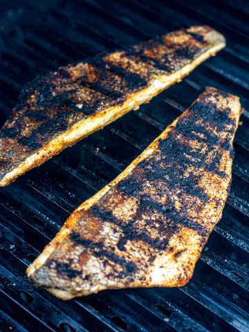 two fillets of Branzino on the grill with a light coating of Jamaican jerk seasoning.