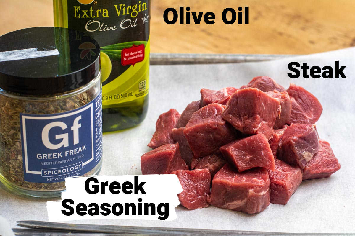ingredient photo showing a pile of steak cubes, greek freak seasoning and oil with labels.