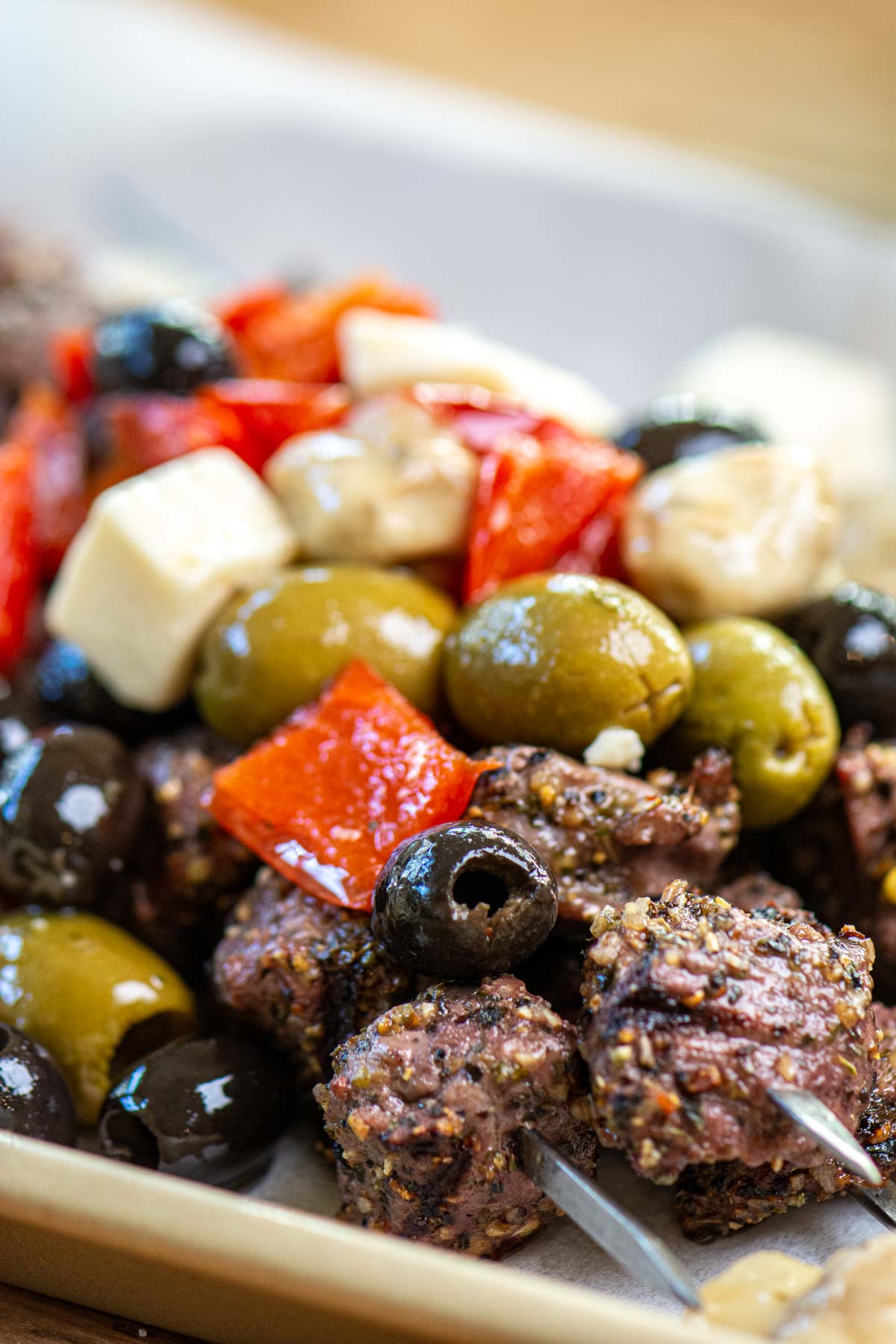 grilled steak bites on metal skewers topped with a greek olive salad mix.