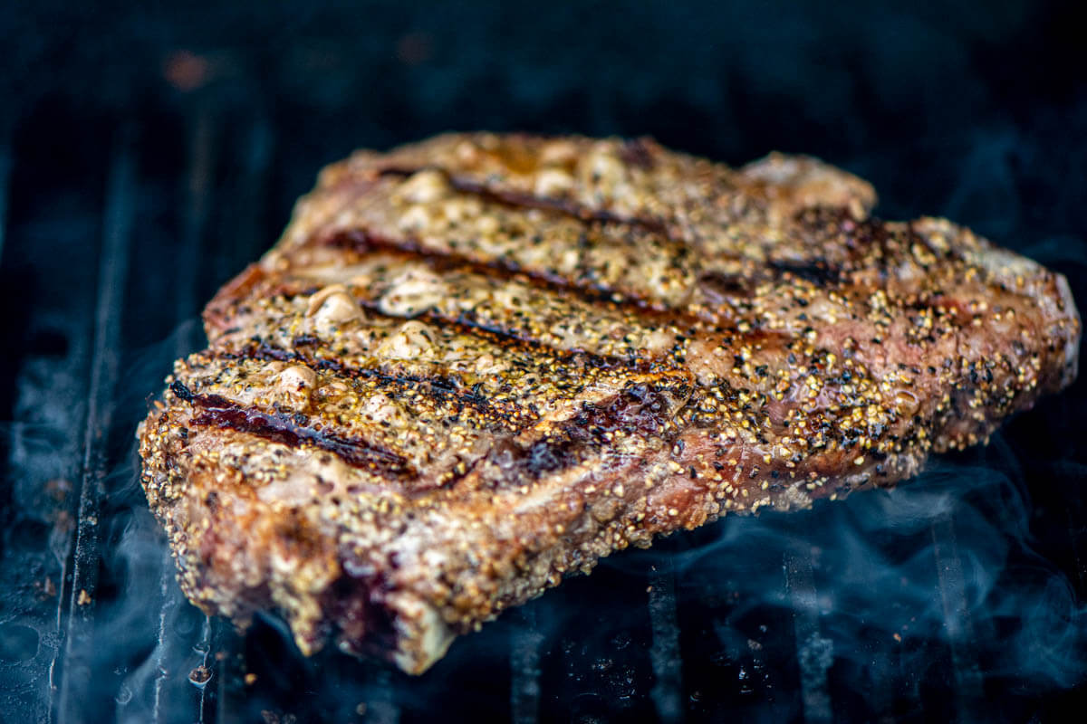 gorgeous grilled t bone on the grill grate with steam coming up around it and a light coating of bourbon salt and pepper.