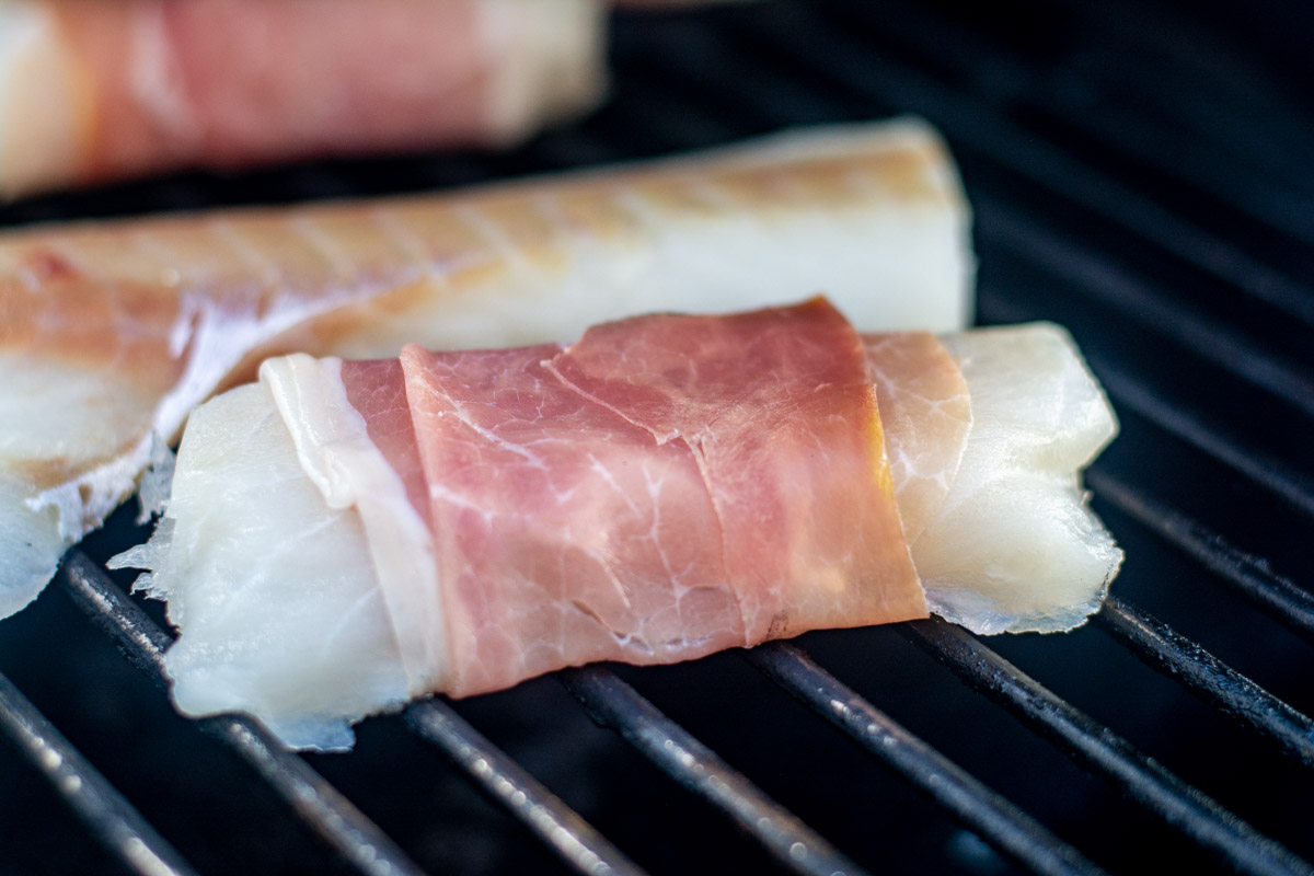 a piece of cod wrapped in the cured met on the grill waiting for the smoke to start up.