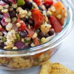 grilled corn and black bean salsa packed with fresh vegetables in a bowl and corn chips on the table.