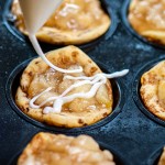 drizzling icing on the apple pie filled cinnamon roll cups in a muffin tin.