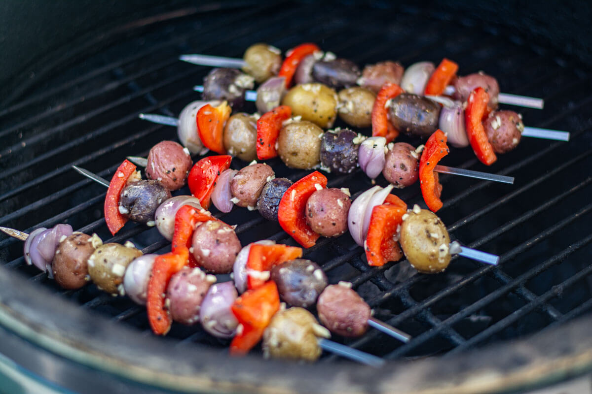 garlic and olive oil coating the peppers, shallots and potatoes on skewers on the grill.