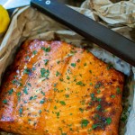 salmon on a sheet pan after grilling with lemons in the background.
