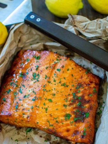 salmon on a sheet pan after grilling with lemons in the background.