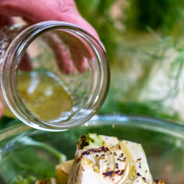 pouring the lemon vinaigrette over the grilled fennel in a glass bowl.