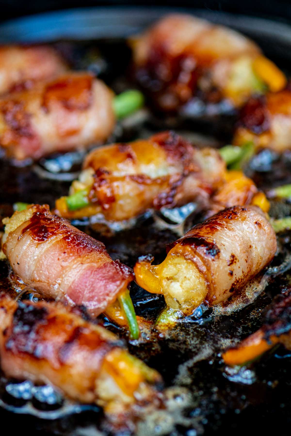 several tater tots wrapped in bacon on the cast iron skillet.