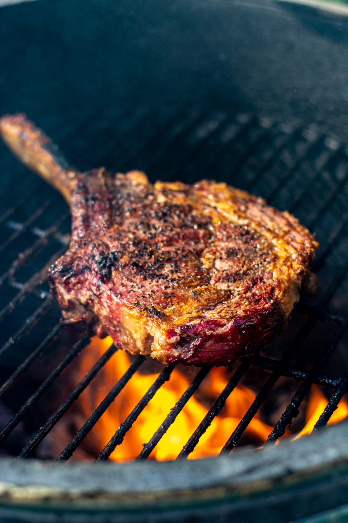 cowboy ribeye on the big green egg grill over direct heat with flames under the steak.