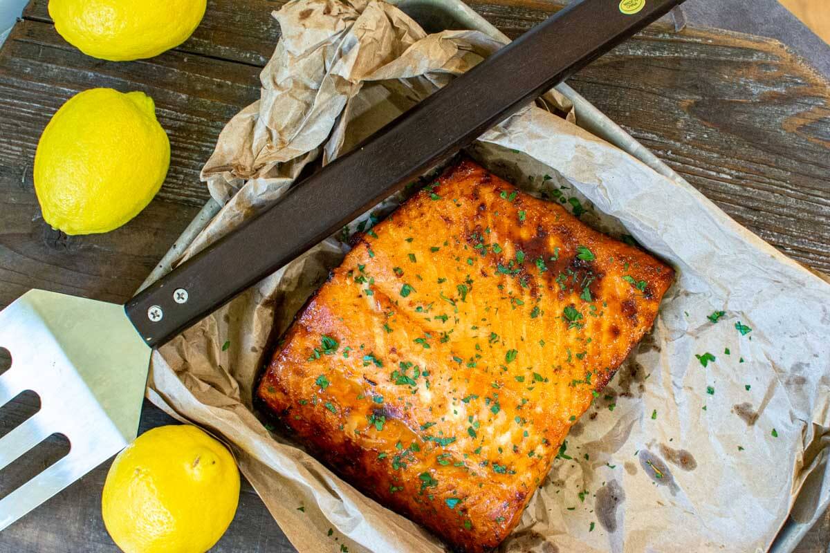 top down view of the grilled salmon and a grilling tool on a rustic cutting board.
