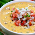 bowl of queso topped with fresh chopped vegetables and tomatoes, cilantro and jalapeño on the table.