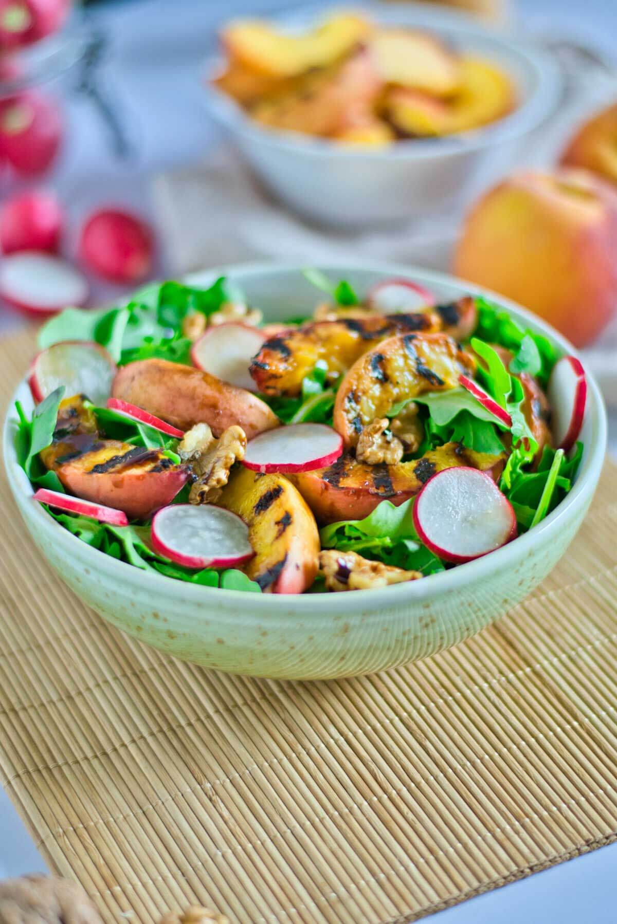 bowl of grilled peaches on a bed of lettuce and topped with radishes and fresh cracked walnuts.