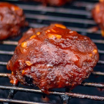 smoked chicken thigh on the grill covered in a thick BBQ sauce.