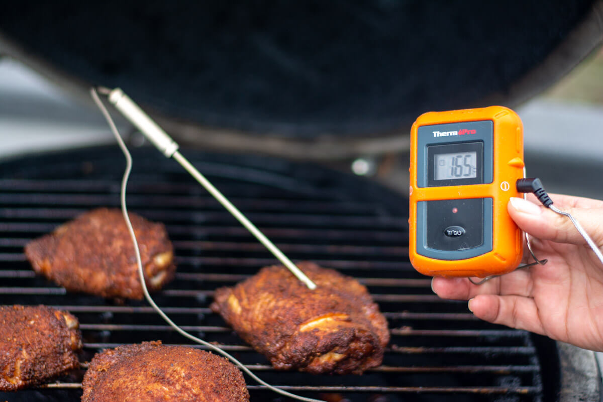 chicken thighs on the grill with the wireless thermometer being held in front.