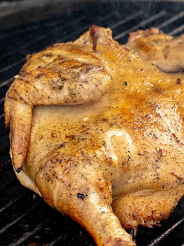 butterflied chicken laid flat on the grill grate with a light smoke coming off of it.