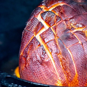 half a ham on a bed of orange slices being smoked on the grill and the score marks are opening up.