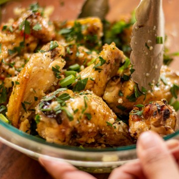 glass bowl filled with chicken wings tossed in garlic, parmesan, green onions and parsley.