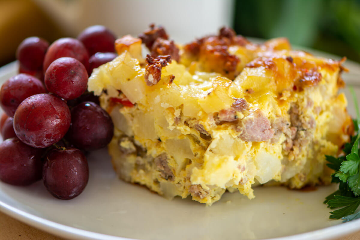 slice of the cooked breakfast casserole on a plate with fresh grapes.