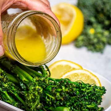 pouring the vinaigrette over the grilled broccolini.