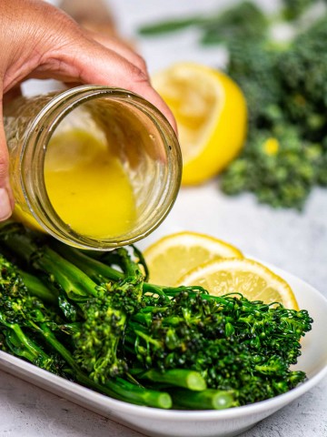 pouring the vinaigrette over the grilled broccolini.