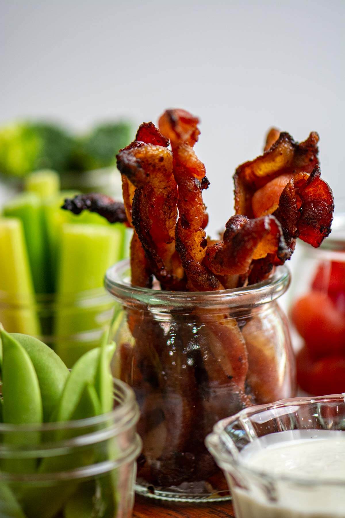 Jar of twisted bacon with fresh vegetables.