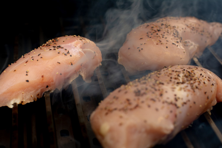 chicken breasts put on a hot GrillGrate with smoke coming up as they quickly sear.