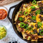 brisket nachos in a cast iron skillet with serving dishes with salsa, guacamole, and olives.