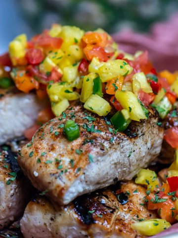 Grilled Mahi Mahi stacked on a sheet pan and topped with pineapple salsa.