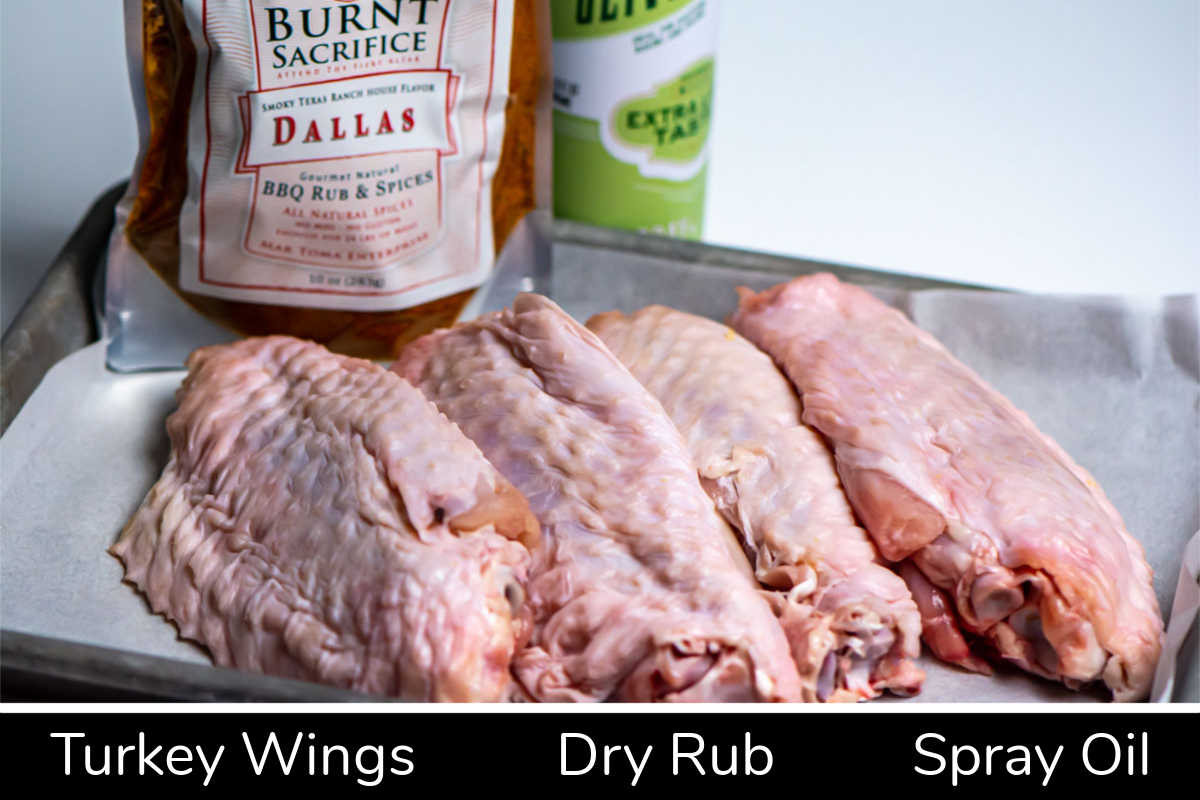 ingredient photo showing the turkey wings, oil, and burnt sacrifice BBQ rub on a small sheet pan with labels.