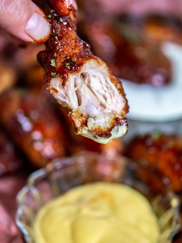 holding a smoked chicken wing with a bite out of it over several dipping sauces.