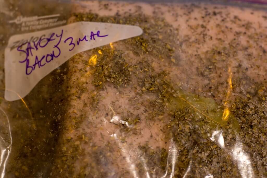 Raw bacon and herb cure in ziplock bag.