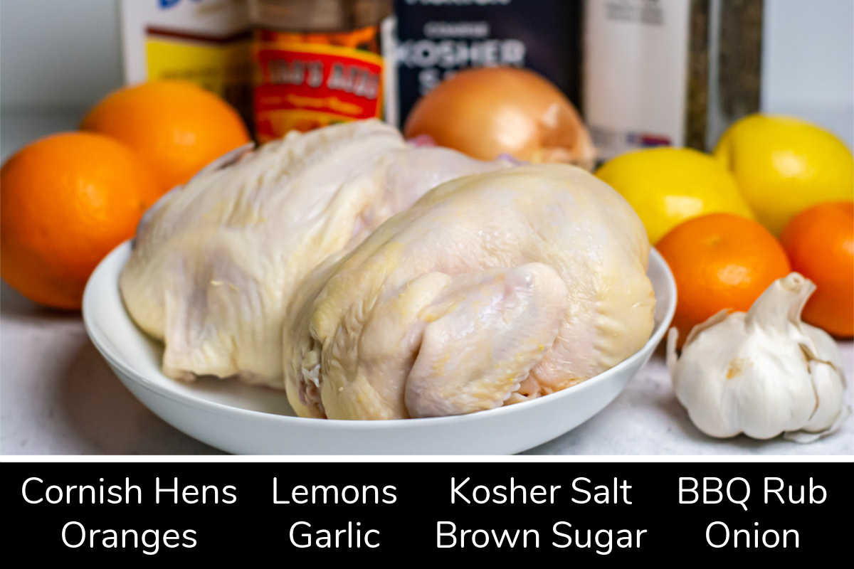ingredient photo showing the Cornish hens, citrus, garlic, and the remaining ingredients on a table with labels.