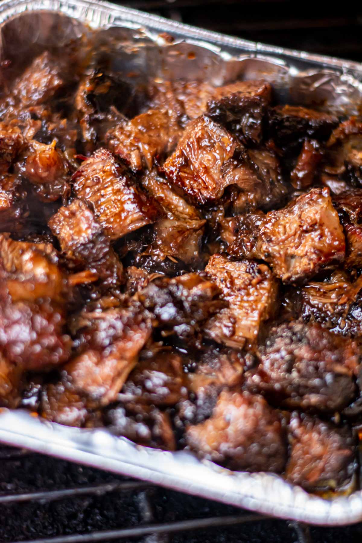 burnt ends in a disposable aluminum pan on the grill with caramelized BBQ sauce.