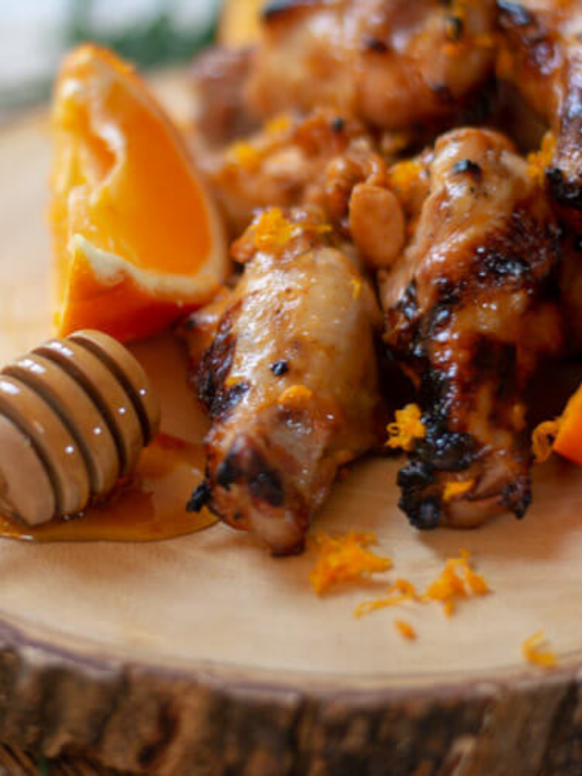 side view of grilled orange and honey sriracha chicken wings on a wooden chopping board.